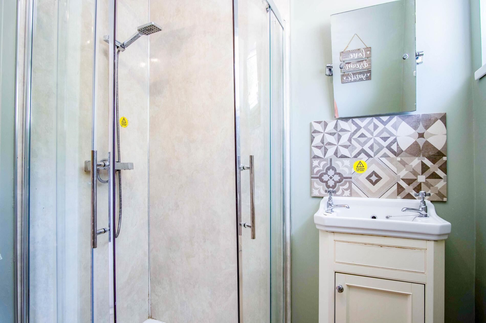 A bathroom with a glass shower enclosure, a sink with a mirror, and a caution sign on the wall.