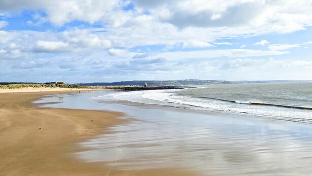 A wide sandy beach with gentle waves, a clear sky, and a distant shoreline with buildings. - Seascape Retreat - 3 Bedroom Flat - Porthcawl (Porthcawl)