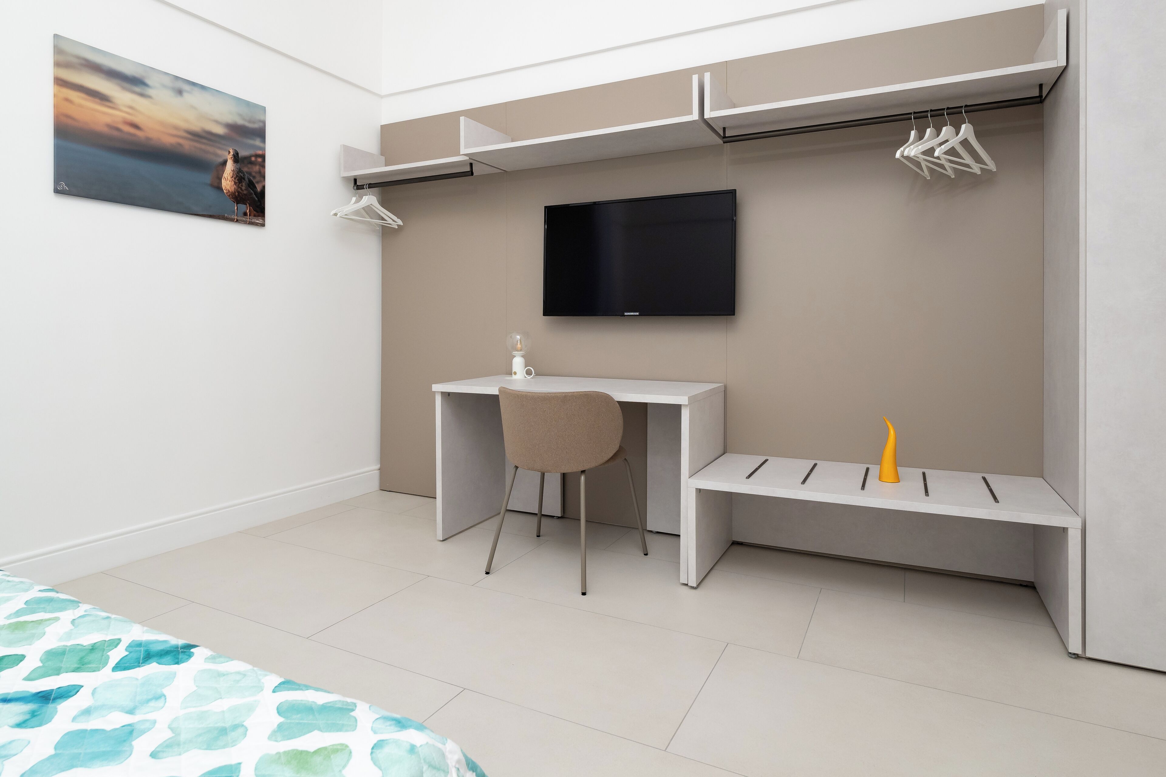 A modern bedroom with a bed, a desk, a chair, a TV, and a bench.