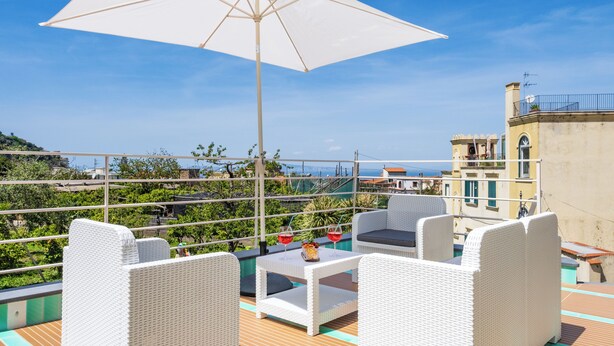 Una terraza con mobiliario blanco de mimbre, una mesa con bebidas y un paraguas grande.
