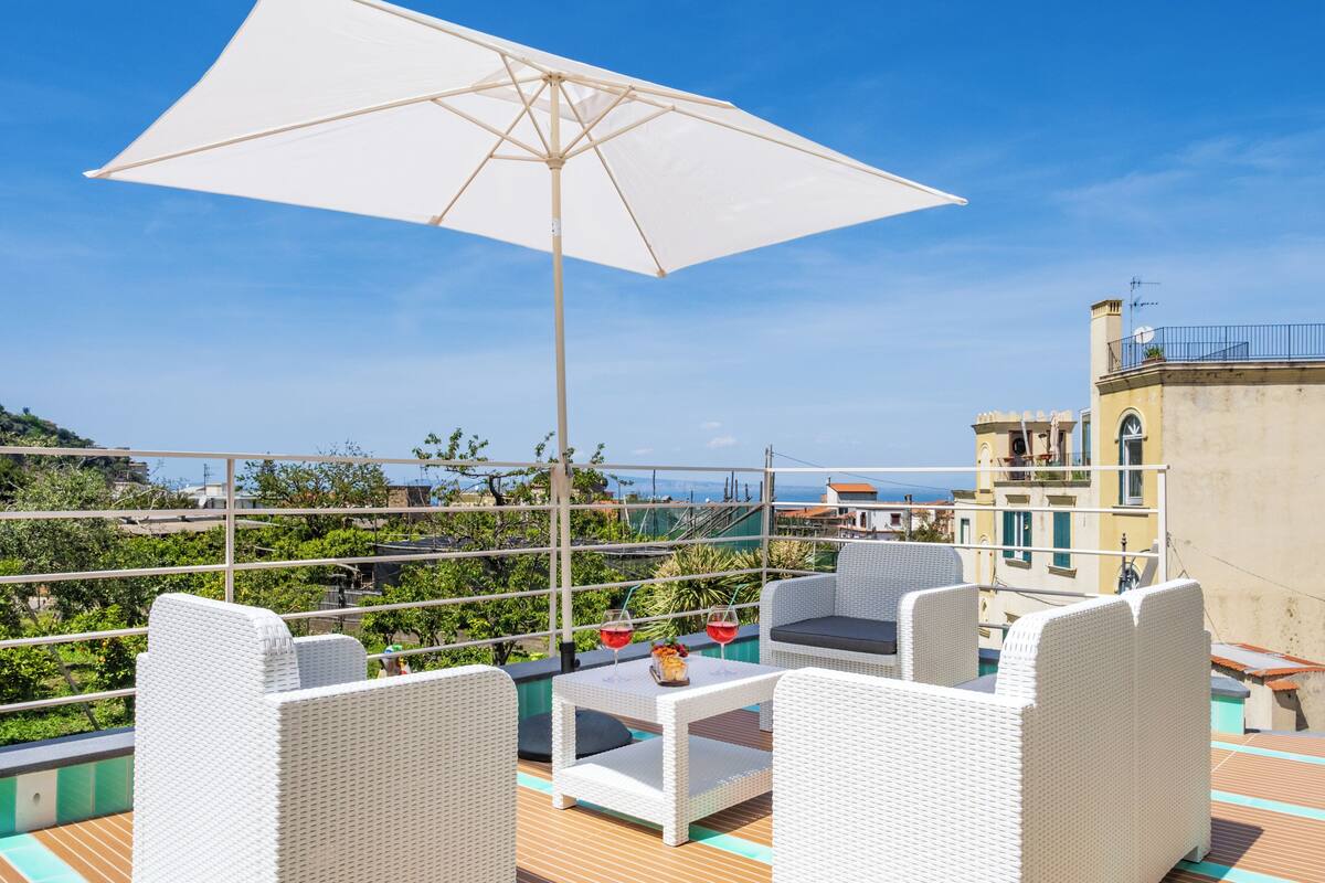Eine Terrasse mit weißen Korbmöbeln, einem Tisch mit Getränken und einem großen Sonnenschirm.