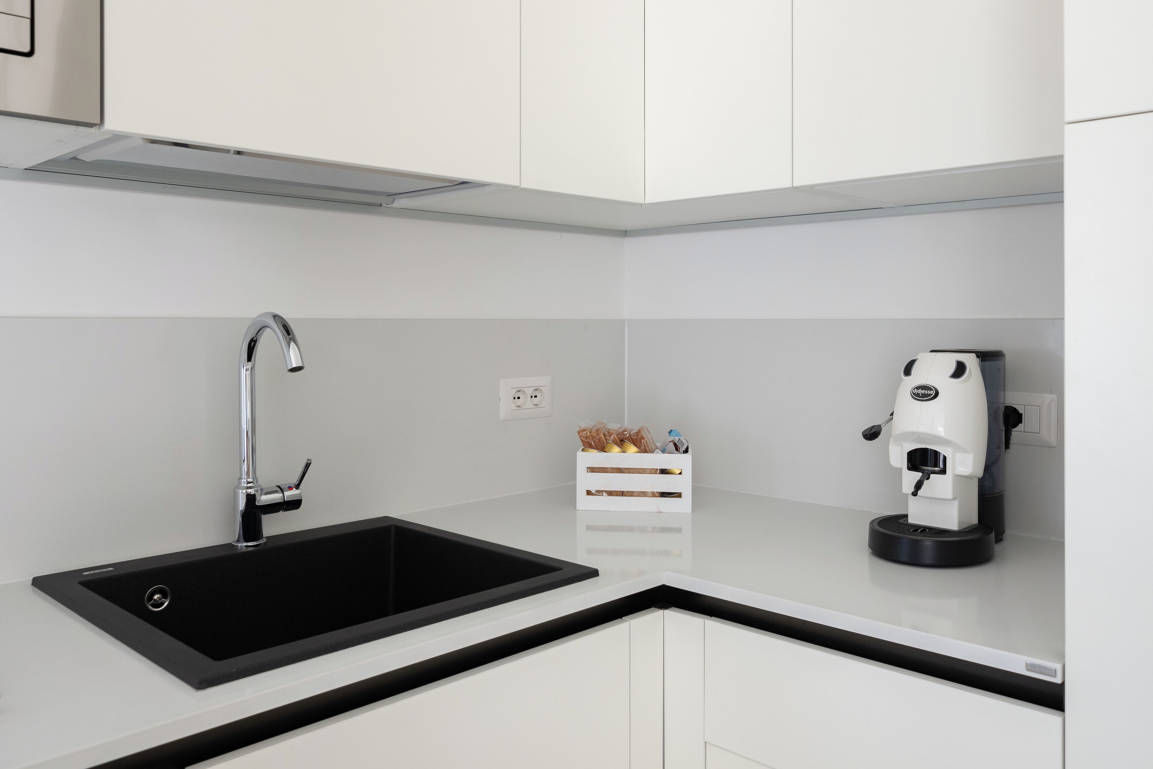 Een moderne keuken met een zwarte spoelbak, witte kastjes en een koffieapparaat.