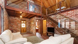 Un salón espacioso con pared de ladrillo, una escalera de madera y un televisor.