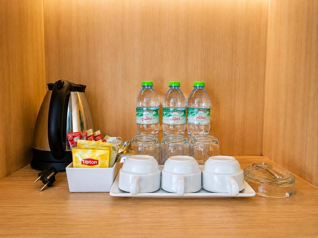 Eine Küchenzeile mit Kaffeemaschine, Lipton Teebeuteln, Wasserflaschen und weißen Tassen auf einer Holzausziehtischplatte.