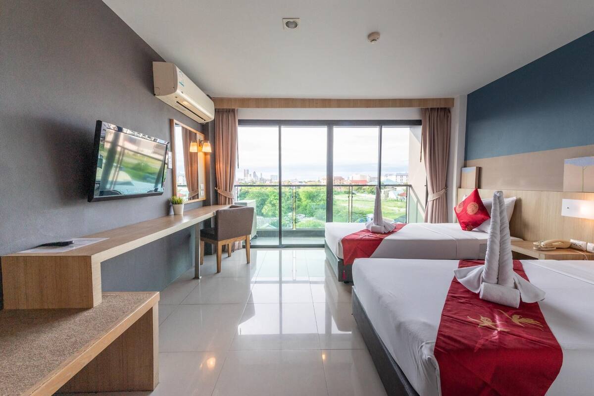 Une chambre d’hôtel équipée d’un lit, d’un bureau, d’une chaise, d’une télévision et d’une grande fenêtre donnant sur la ville.