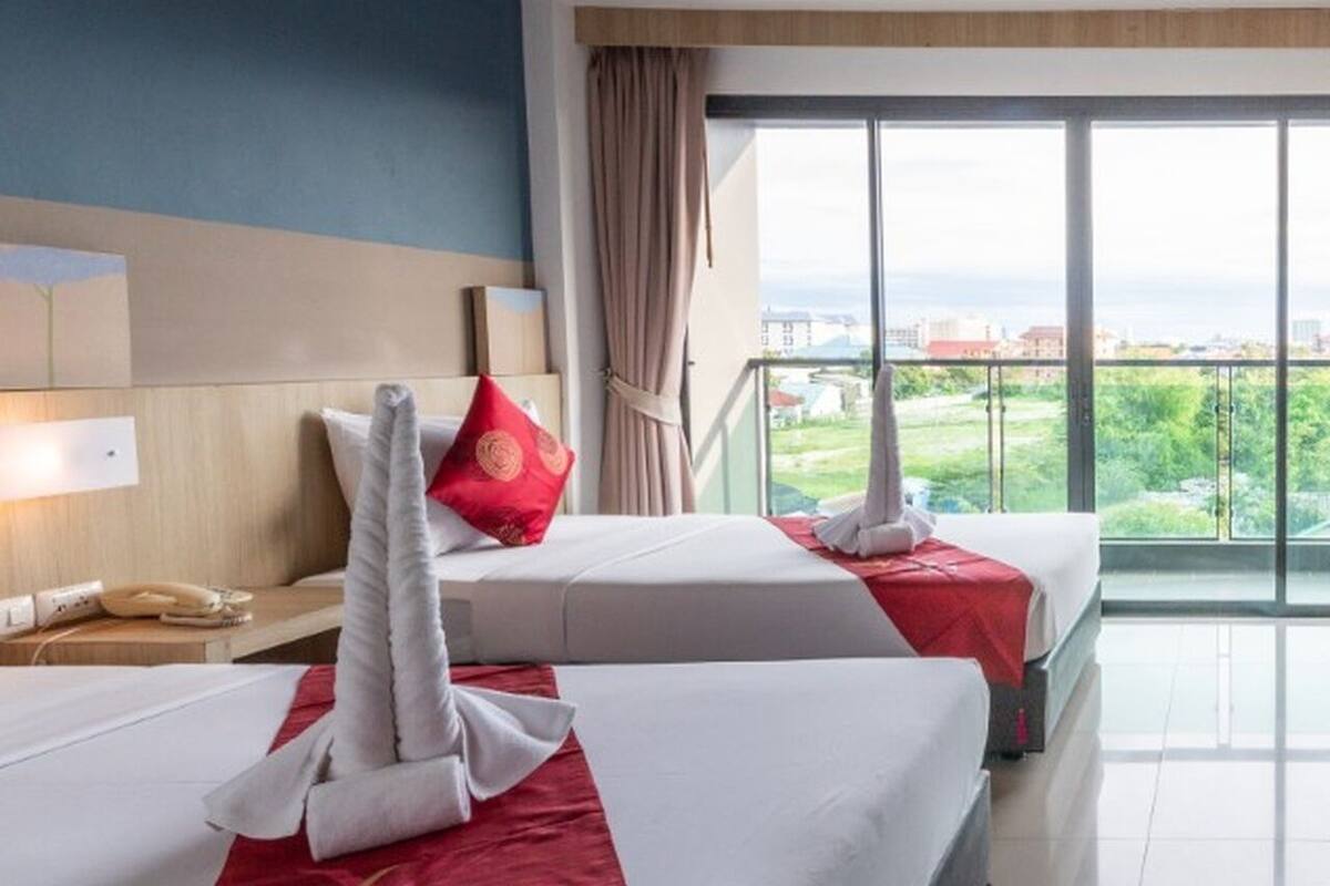 Une chambre d’hôtel avec deux lits, un bureau, un téléphone et une grande fenêtre donnant sur un beau paysage.