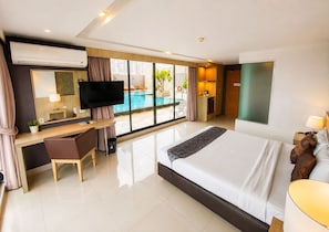A modern hotel room with a large bed, a desk with a chair, a television, and a view of an outdoor swimming pool. - Arawana Regency South Pattaya (Pattaya)