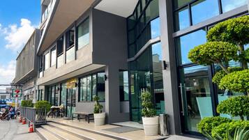 Un edificio moderno con techo plano, ventanas amplias y un área de entrada pavimentada con escalones y plantas en macetas.