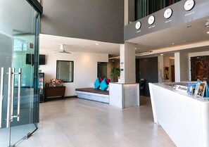 Un moderno vestíbulo de hotel con un mostrador de recepción, zona de estar y un ascensor de vidrio.