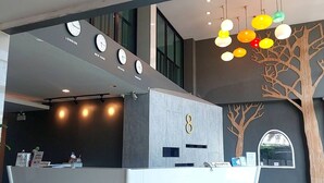 Un espace d’accueil au design moderne, comprenant un comptoir de réception, des horloges indiquant différents fuseaux horaires et un mur décoratif arboré.