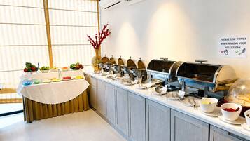 A buffet setup with multiple food stations, a sign instructing to use tongs, and a decorative vase with red flowers.