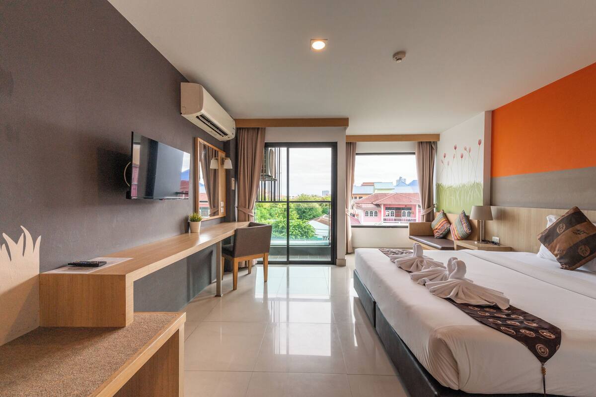 Une chambre d’hôtel équipée d’un lit, d’un bureau, d’une chaise, d’une télévision et d’une fenêtre donnant sur des immeubles.
