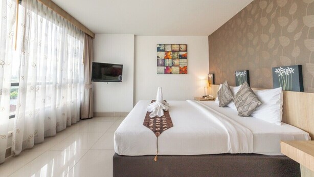 Une chambre d’hôtel dotée d’un grand lit, d’un téléviseur à écran plat fixé au mur, d’une œuvre d’art décorative et d’une fenêtre ornée de rideaux légers.