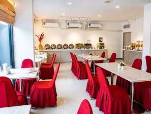 Un comedor con sillas y mesas rojas, una cocina al fondo y unidades de aire acondicionado en el techo.