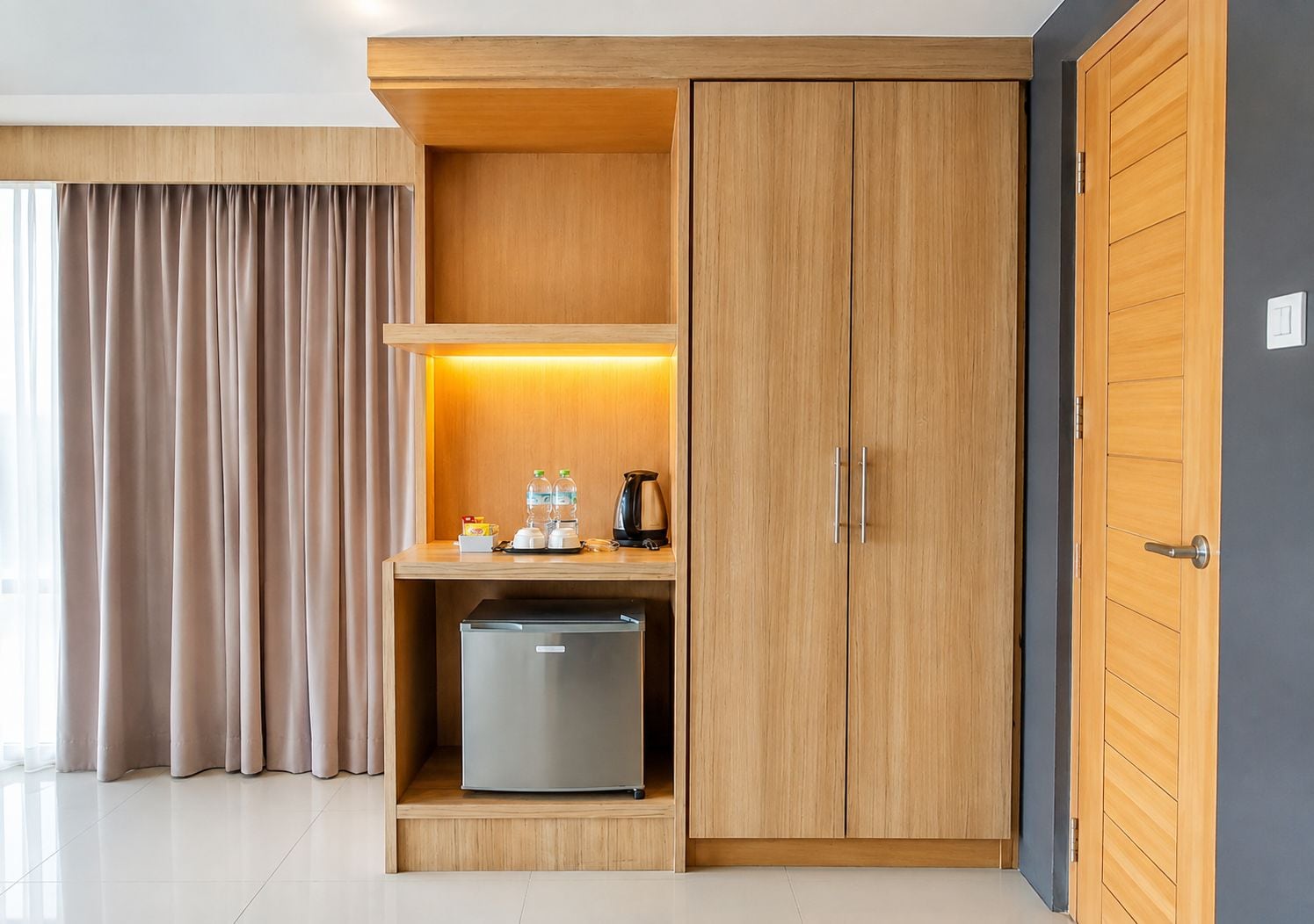 Ein modernes Hotelzimmer mit einem Holzschrank, einer Minibar und einem kleinen Kühlschrank.