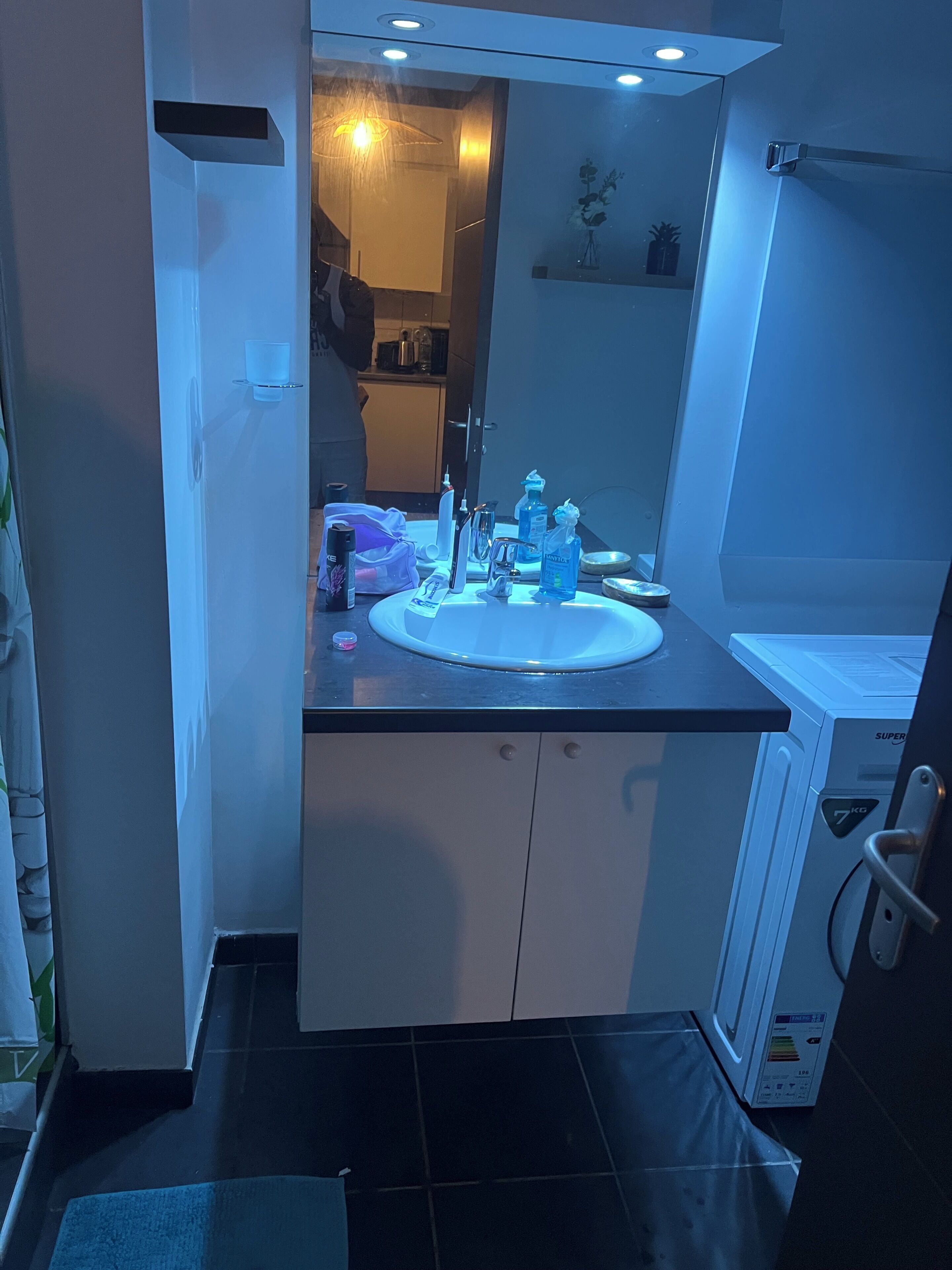 A modern bathroom with a large mirror, a sink, and a toilet. There are toiletries on the sink counter.