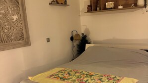 A neatly made bed with a floral bedspread, a wall-mounted shelf with decorative items, and a wall carving. - Bora bora studio vacation (Bora-Bora)