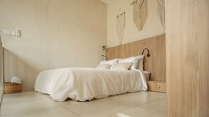 Quarto com cama, cabeceira de madeira, decoração de macramé na parede e cesta de vime com lenços.