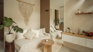 Uma sala de estar moderna com um sofá, uma mesa de centro redonda de madeira, um painel de macramé e um armário de madeira com objetos decorativos.