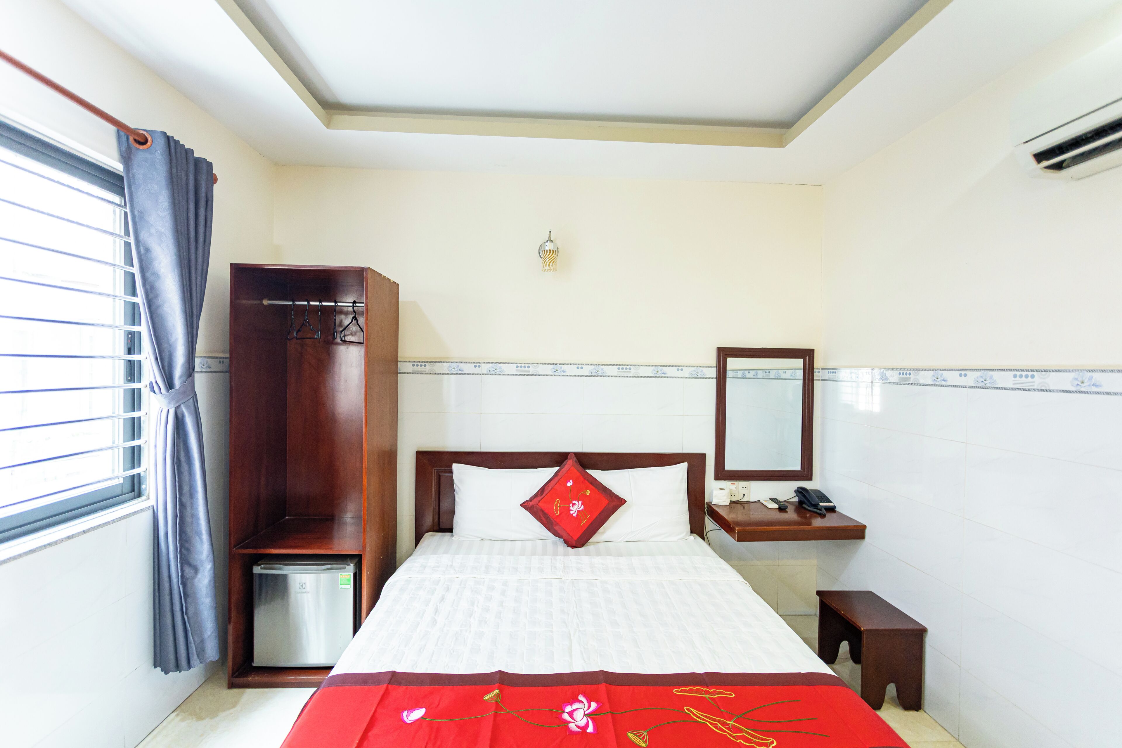 Une chambre d’hôtel comprenant un lit, une armoire, une table de chevet avec un téléphone et une fenêtre avec des rideaux.