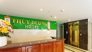 Een hotel receptie met een groen bord, een houten receptiebalie en een lift.