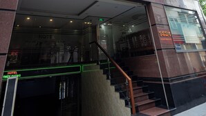 Een hotelentree met een trap die naar de deur leidt, een bord boven de deur en een reflectie op de glazen gevel.