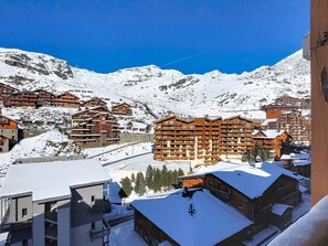 Un poble envoltat de neu a la muntanya, amb edificis de fusta, incloent un hotel gran amb diversos balcons i una telecabina al fons.