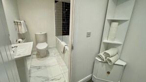 Moderni kylpyhuone, jossa on wc, pesuallas ja lasiseinällä varustettu suihku.