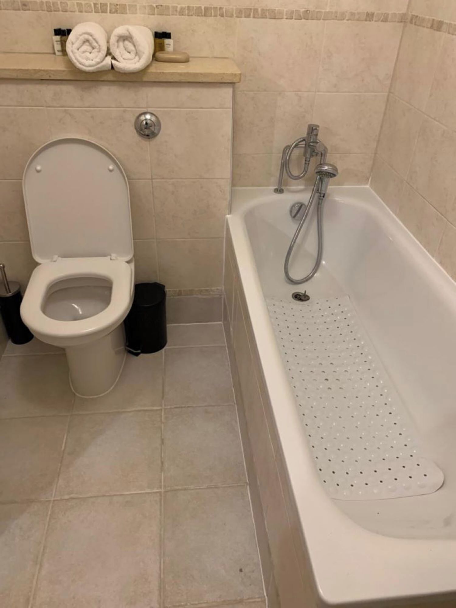 Une salle de bain comprenant des toilettes, une baignoire avec pomme de douche et un porte-serviettes avec des serviettes.