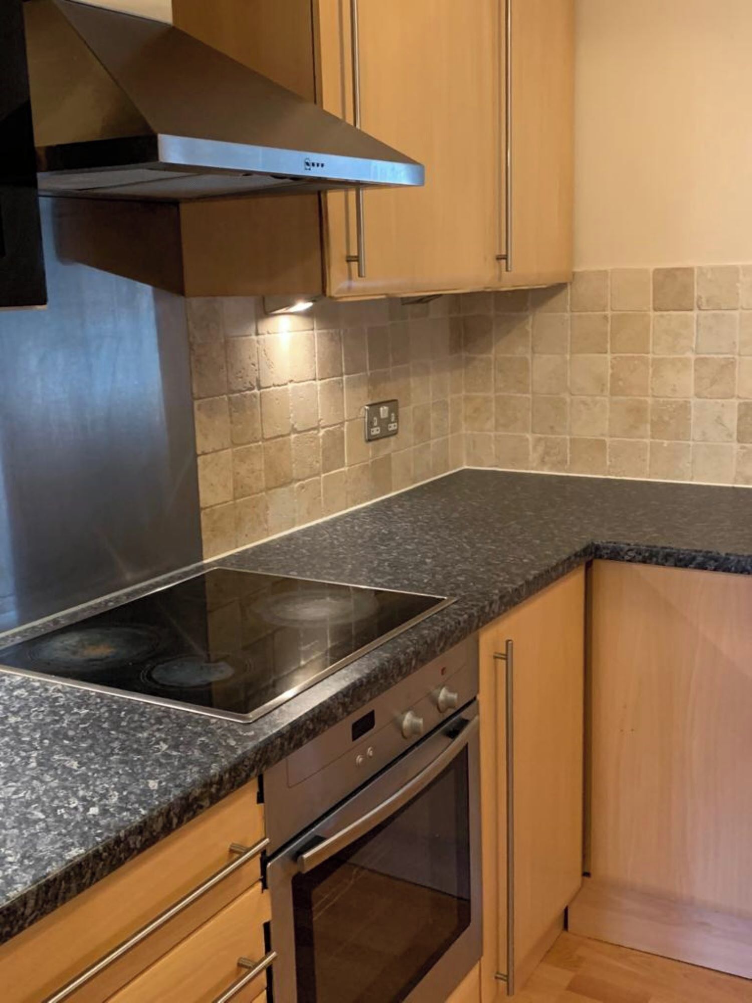 A kitchen with a stainless steel range hood, a built-in oven, and a granite countertop.