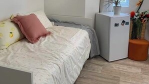 Une chambre avec un lit, un petit réfrigérateur blanc, une fenêtre avec des rideaux et un élément décoratif mural.