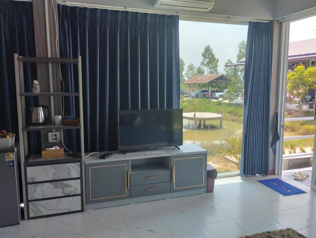 Una sala de estar con un televisor sobre un mueble gris, un estante con objetos y vistas a un patio con mesa y sillas.
