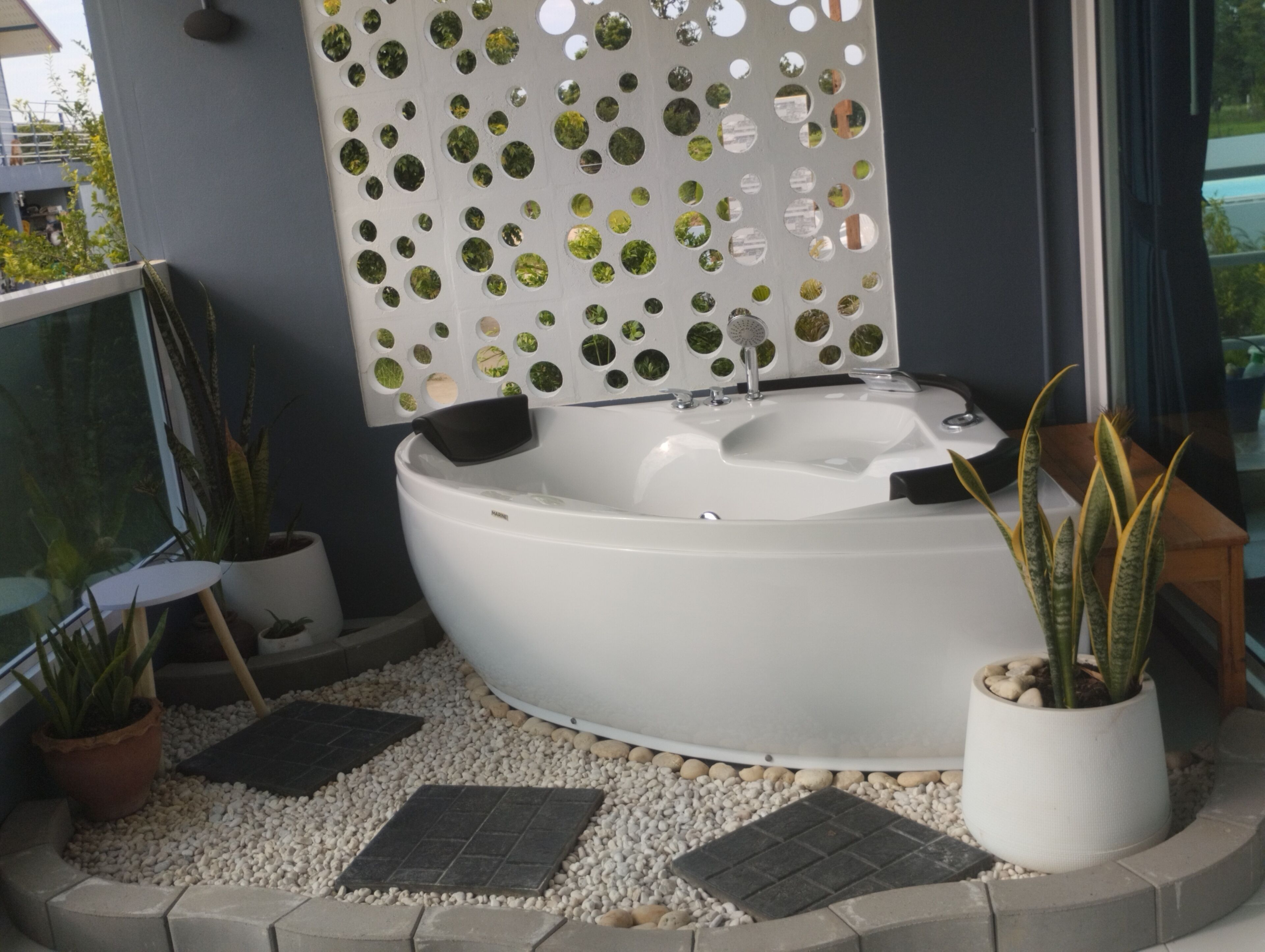 A spa area with a hot tub, a decorative wall with circular cutouts, and potted plants.