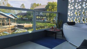 A modern bathroom with a large bathtub, a window with a view of a garden and a house, and a decorative wall with circular mirrors.