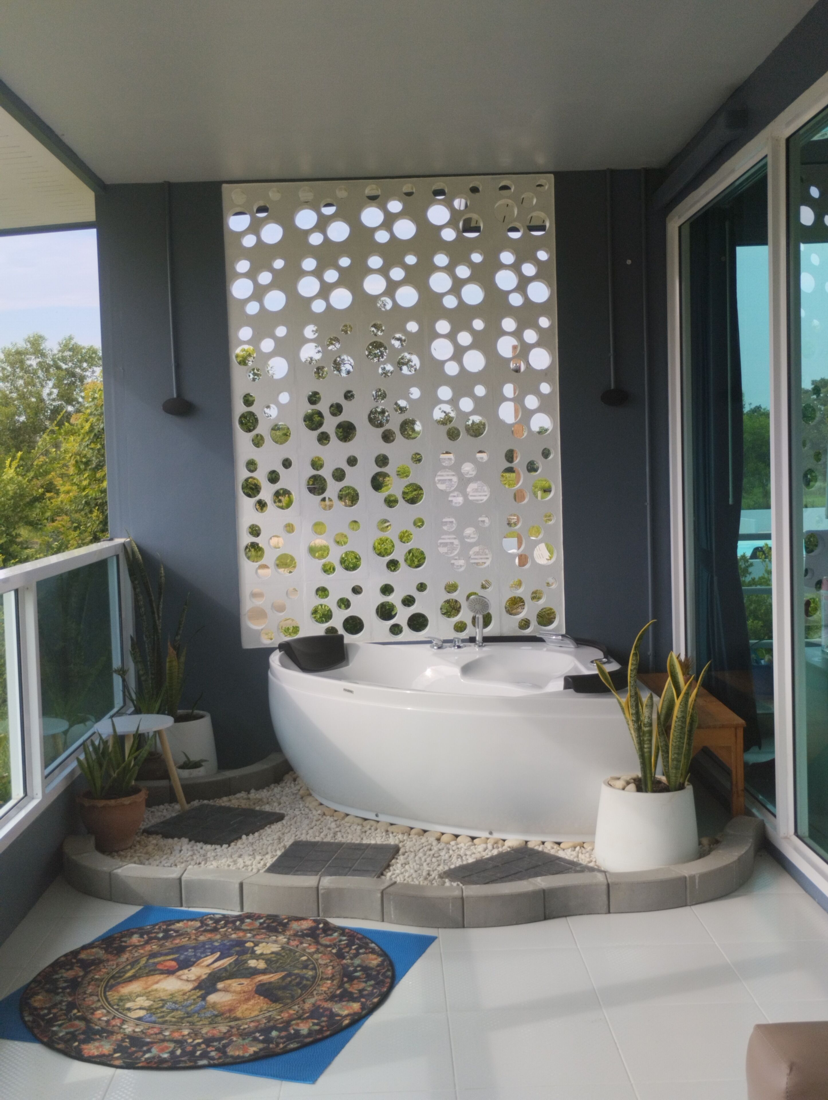 Un baño moderno con una bañera independiente, un revestimiento decorativo con círculos y una planta en maceta.