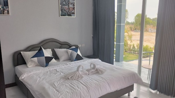 A spacious bedroom with a large bed, a view of the outdoors, and a cityscape painting on the wall.