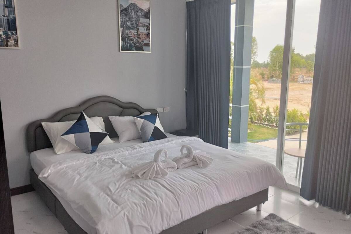 A spacious bedroom with a large bed, a view of the outdoors, and a cityscape painting on the wall.