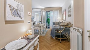 Un espace de vie compact comprenant un coin repas, une chambre avec un lit et une table de chevet, et une cuisine visible au fond.