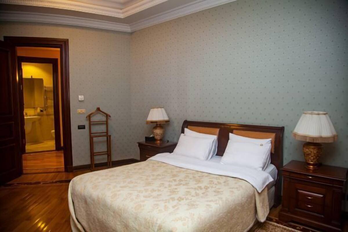 A neatly arranged bedroom with a large bed, two bedside tables with lamps, and a wooden ladder against the wall.