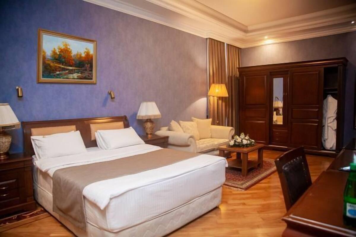 A hotel room with a large bed, a sofa, a wooden table, and a wardrobe.