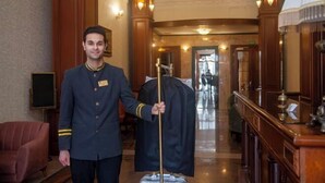 Un vestíbulo de hotel con paneles de madera, una araña y un perchero con abrigo negro.