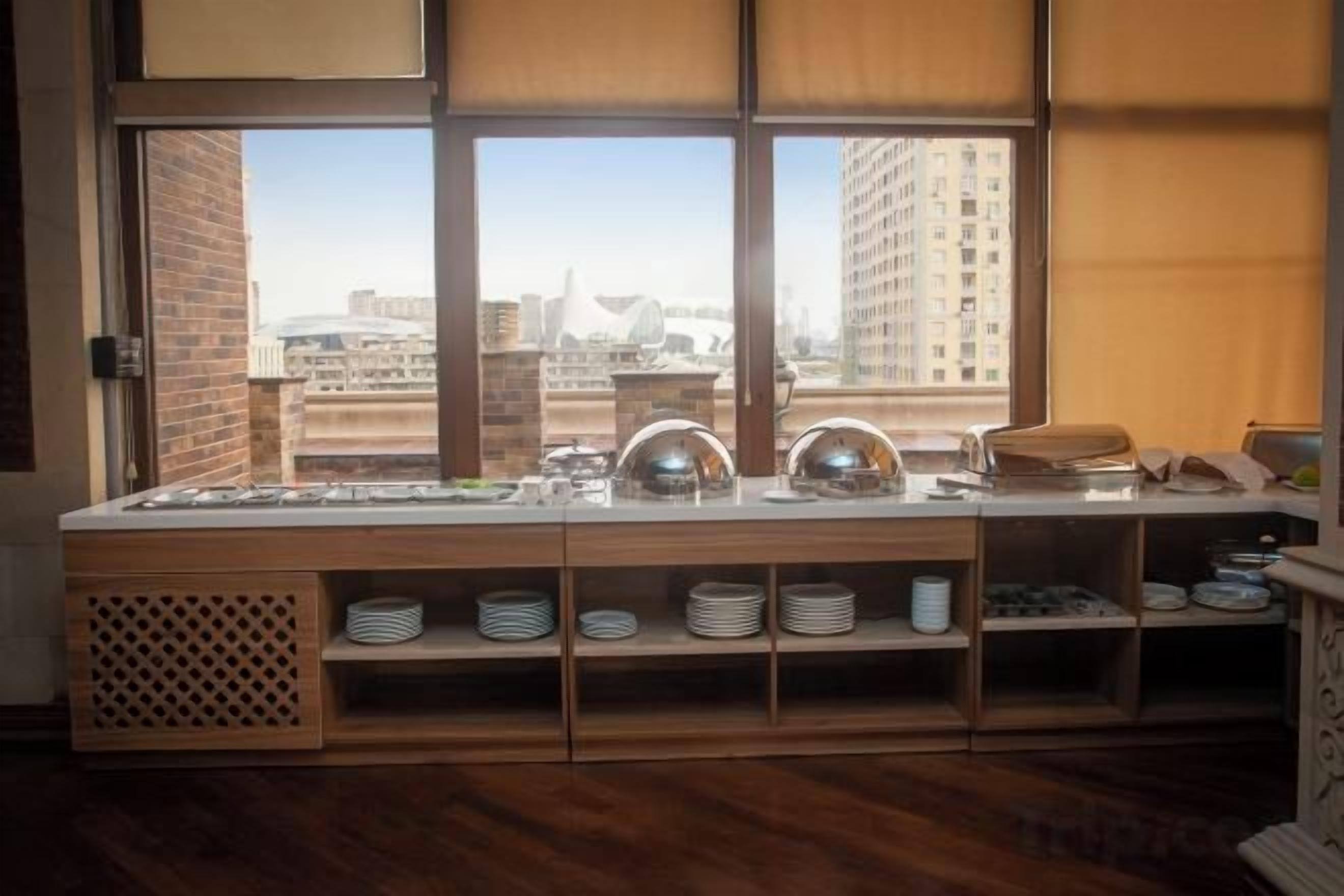 A buffet setup with a view of tall buildings through large windows.