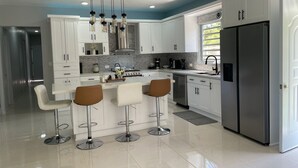 A modern kitchen with white cabinets, a stainless steel refrigerator, and a central island with bar stools. - Welcome to Casa Cangrejo, your perfect escape in Puerto Plata, DR (Sosúa)