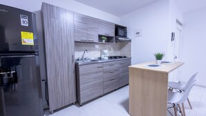 A modern kitchen with grey cabinetry, a black refrigerator, a microwave, and a small dining area with a wooden table and two white chairs. - Beautiful Apartasuite in the best location (Cartago)