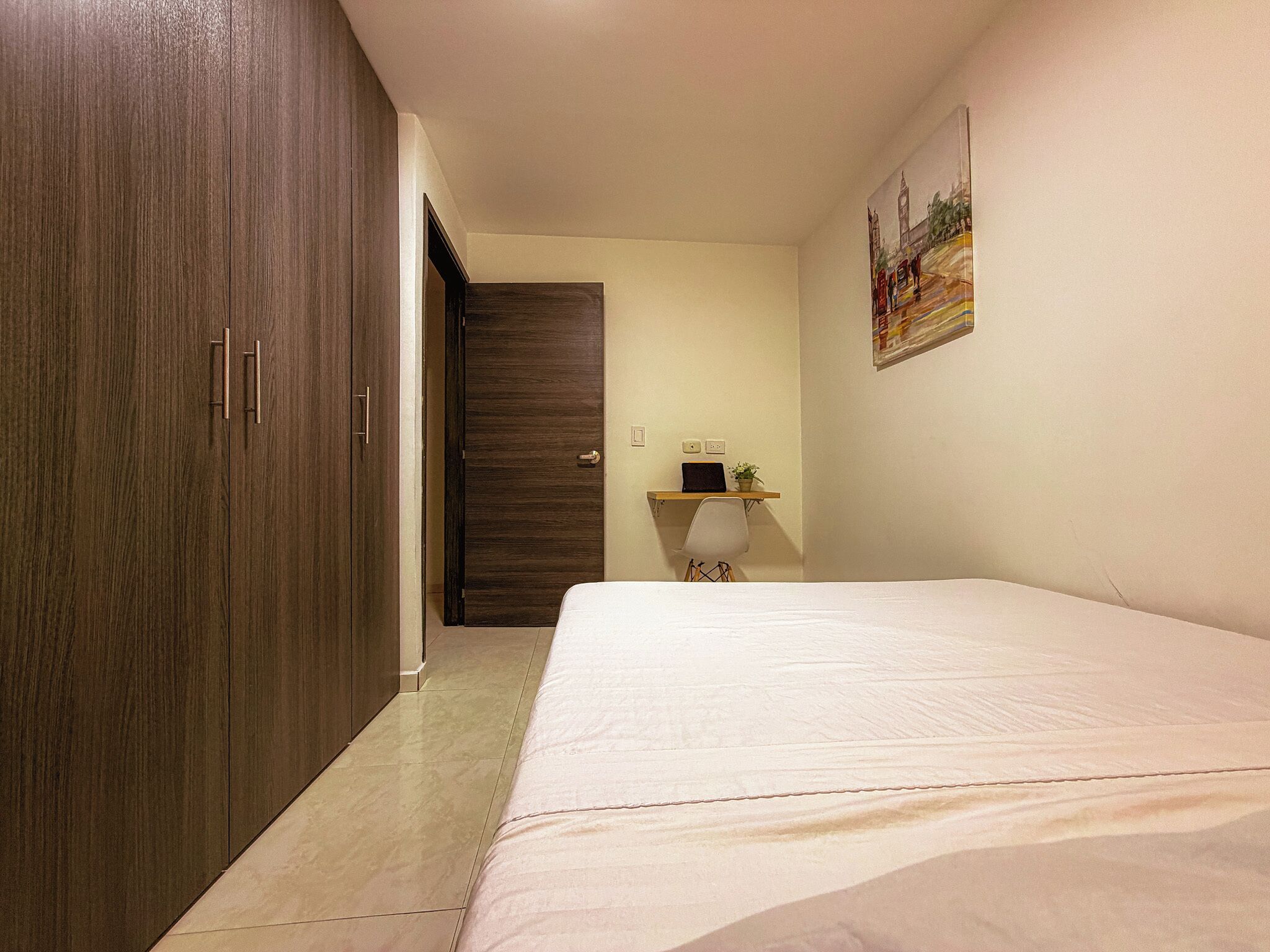 A bedroom with a bed, a wardrobe, a desk with a chair, and a door.