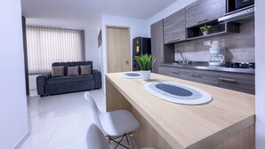 A modern kitchen with a wooden countertop, a built-in microwave, and a coffee maker. There is a dark-colored sofa in the adjacent living area. - Beautiful Apartasuite in the best location (Cartago)