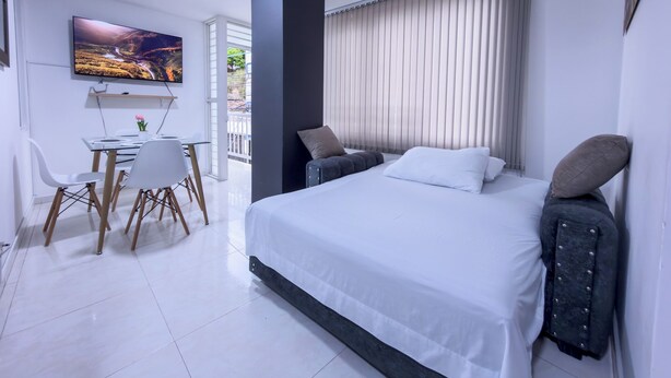 A modern bedroom with a large bed, a desk with chairs, a TV, and a balcony with a view. - Beautiful Apartasuite in the best location (Cartago)