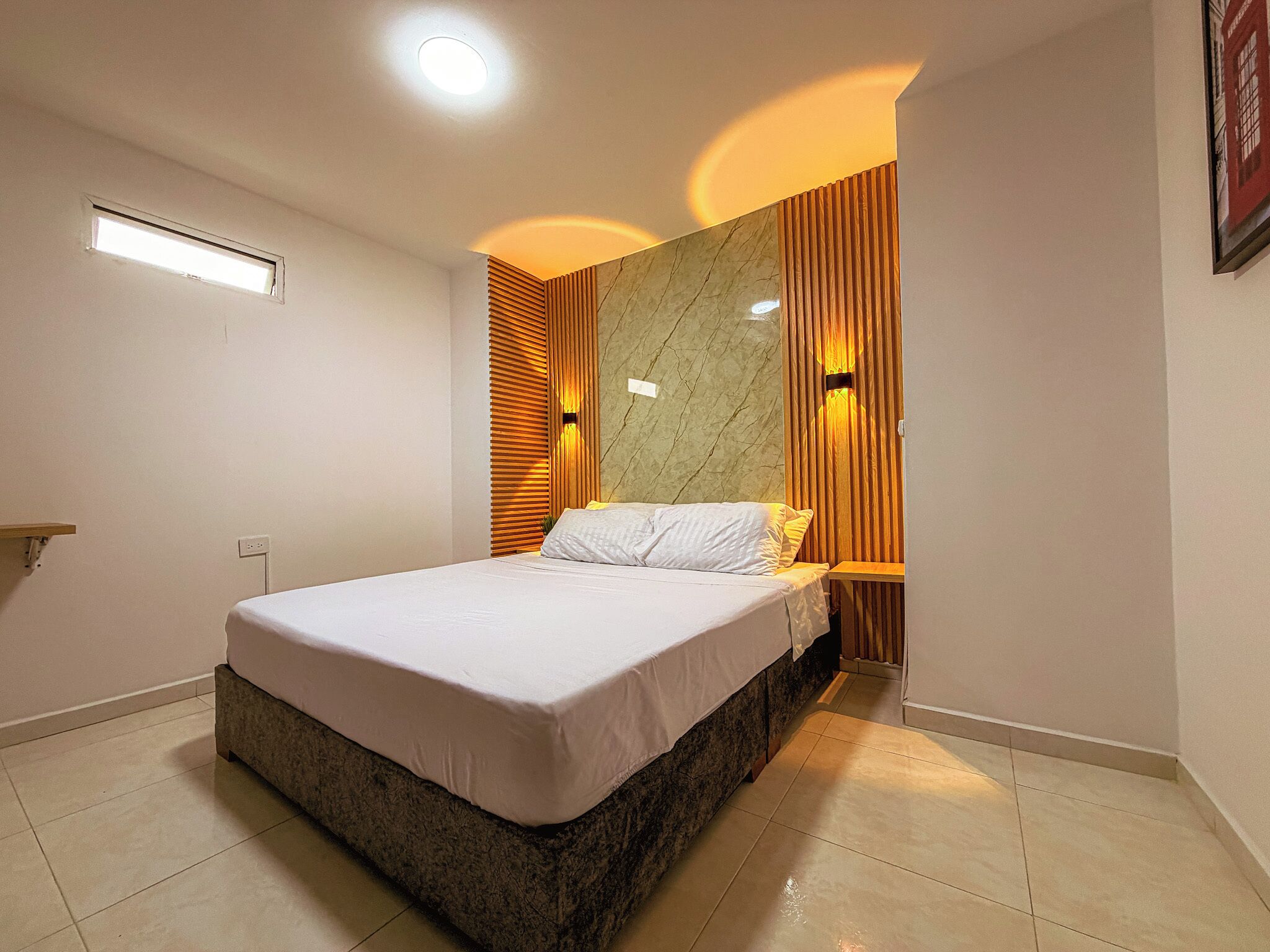 Un dormitorio moderno con cama, panel de madera, pared de acento de mármol e iluminación empotrada en el techo.