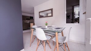 A modern dining area with a glass table, white chairs, and a potted plant. - Beautiful Apartasuite in the best location (Cartago)