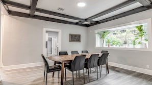 Un comedor con una mesa de madera y sillas negras, una ventana con plantas y una puerta blanca.